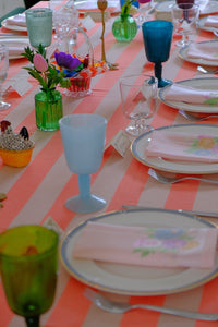 Vibrant birthday tablescape with pastel glassware, floral napkins, and colourful decorations set on a striped tablecloth.