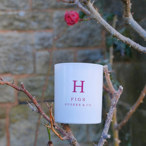 A Huskke & Co Figs candle nestled in twigs with a delicate rose in the background, possibly at an event, showing that candles make good wedding gifts.