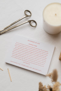 A candle care card advising on burning candles next to a candle and wick trimmer