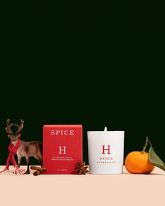 Huskke & Co Spice Natural Wax Candle in a white glass jar alongside a festive red box, cinnamon sticks, and a cosy reindeer ornament. A warming Christmas candle with rich spice and citrus notes.